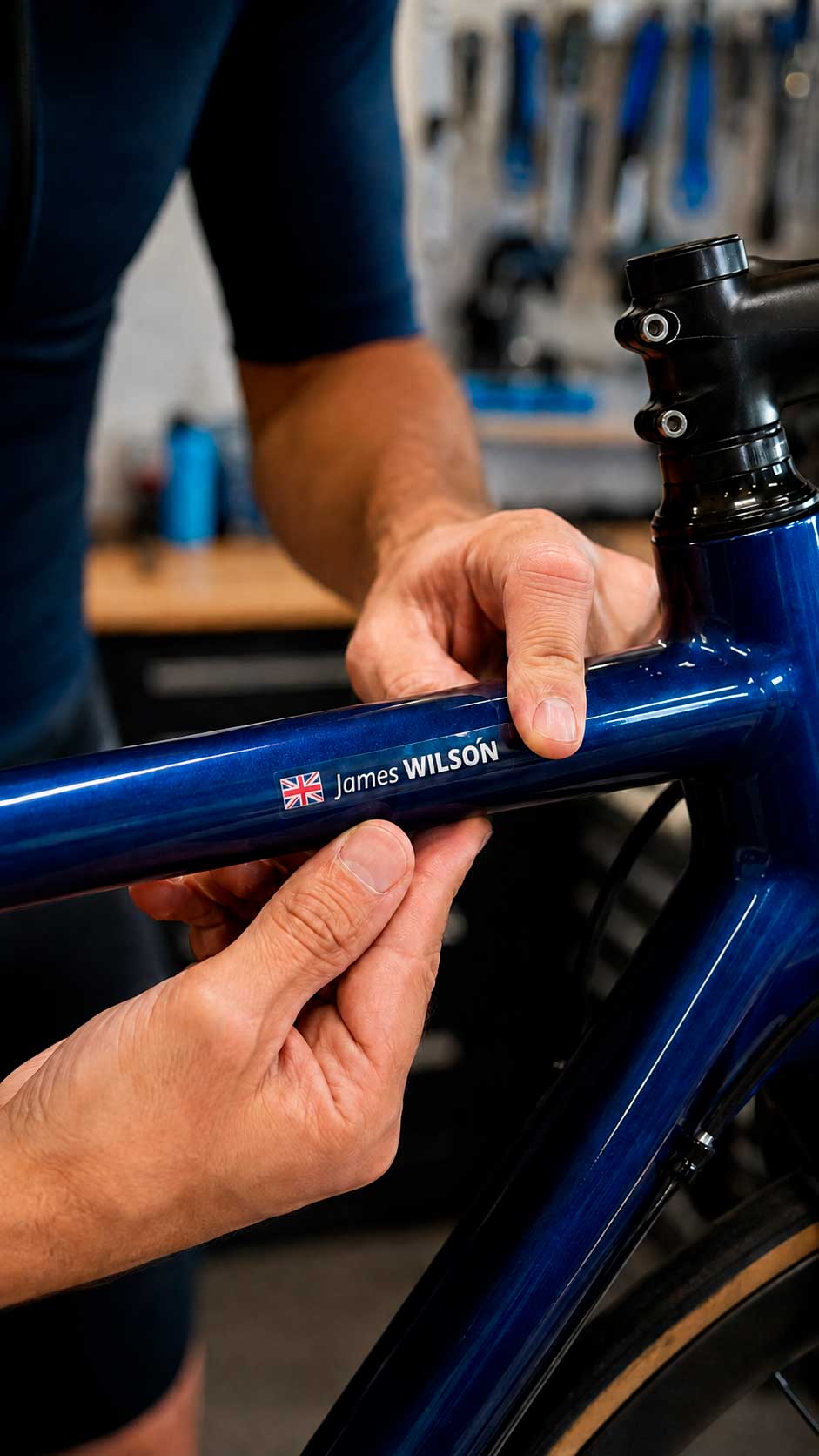 Cyclist smoothing a personalised name sticker with a UK flag onto a blue bike’s top tube