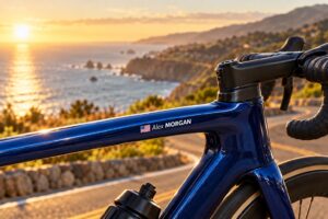 Blue road bike with an Alex MORGAN name sticker and USA flag beside a coastal road